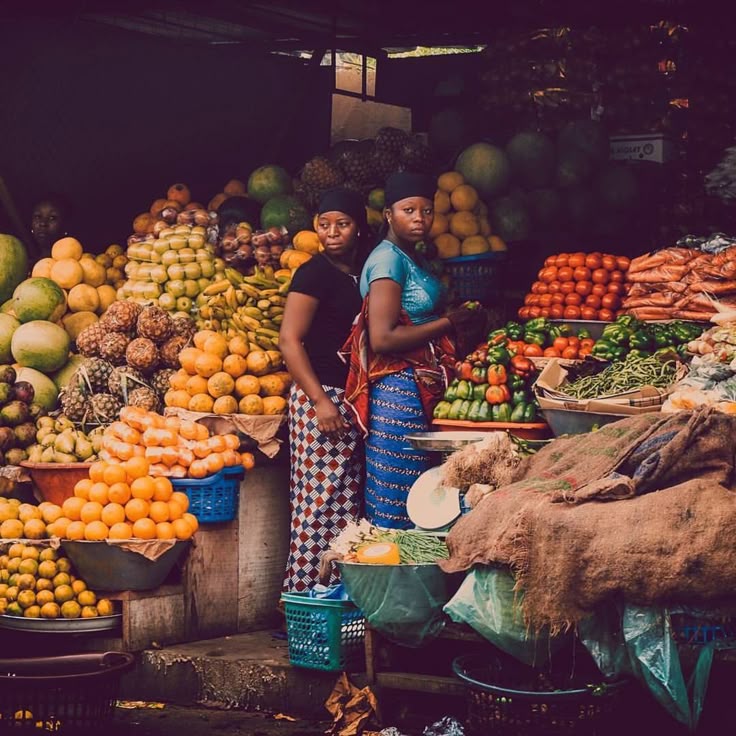 Vendedoras num mercado local, rodeadas de fruta e produtos frescos